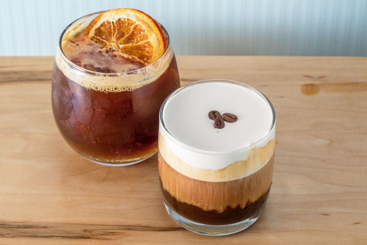 Two coffee drinks in glasses on a wooden table.