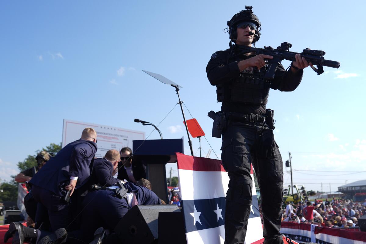 On an outdoor stage, Trump is covered by Secret Service agents after a shooting.