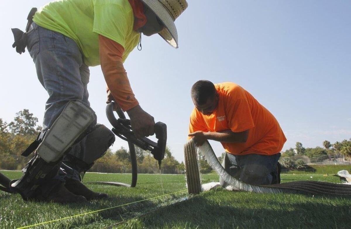 Javier Acosta, left, and installation foreman Pablo Vasquez inlay lines (using glue and white turf) for the goalie box on a field at Leo Mullen Sports Park.