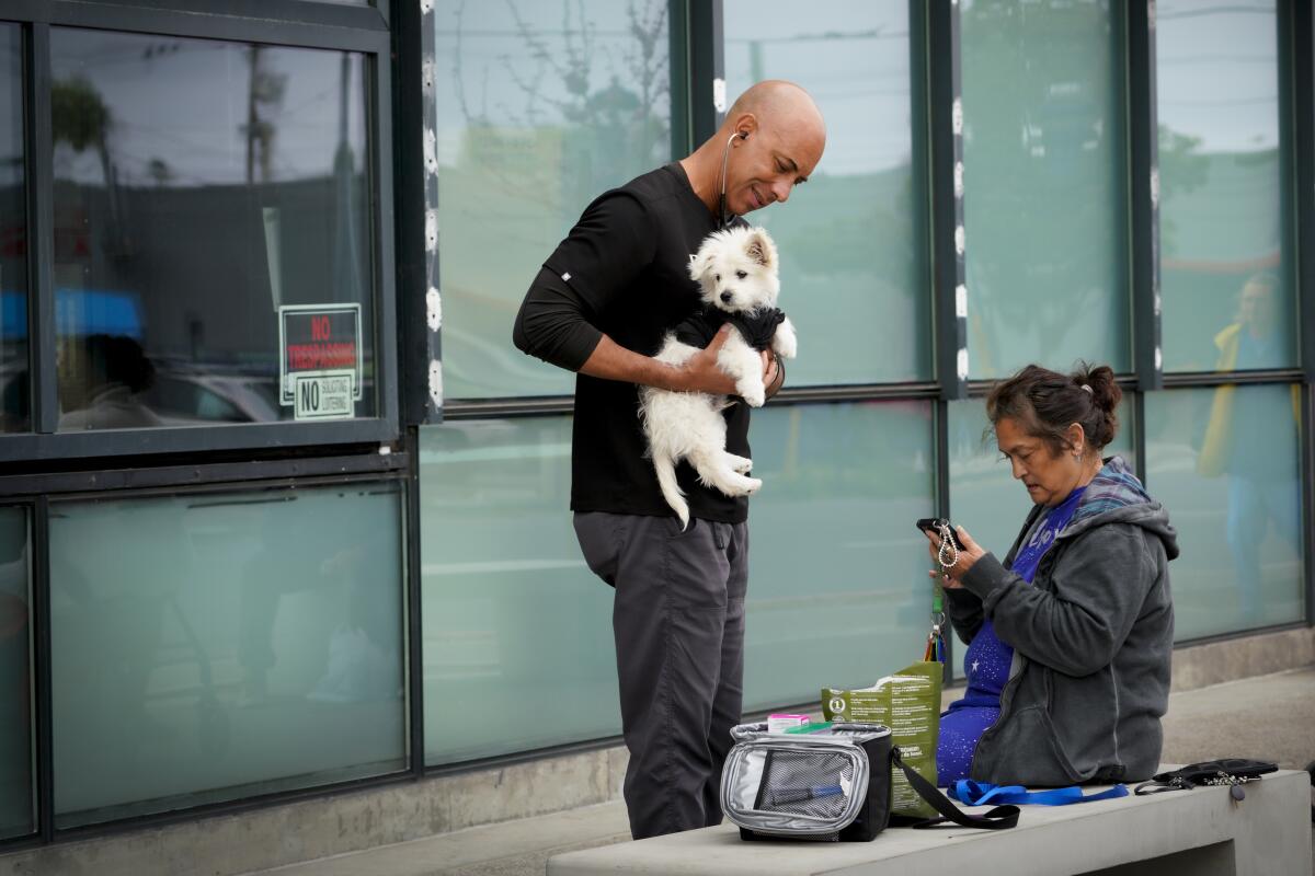 Dr. Kwane Stewart listened to a dog's heart while her owner, Terry Gauci sits nearby in San Diego on March 31, 2022