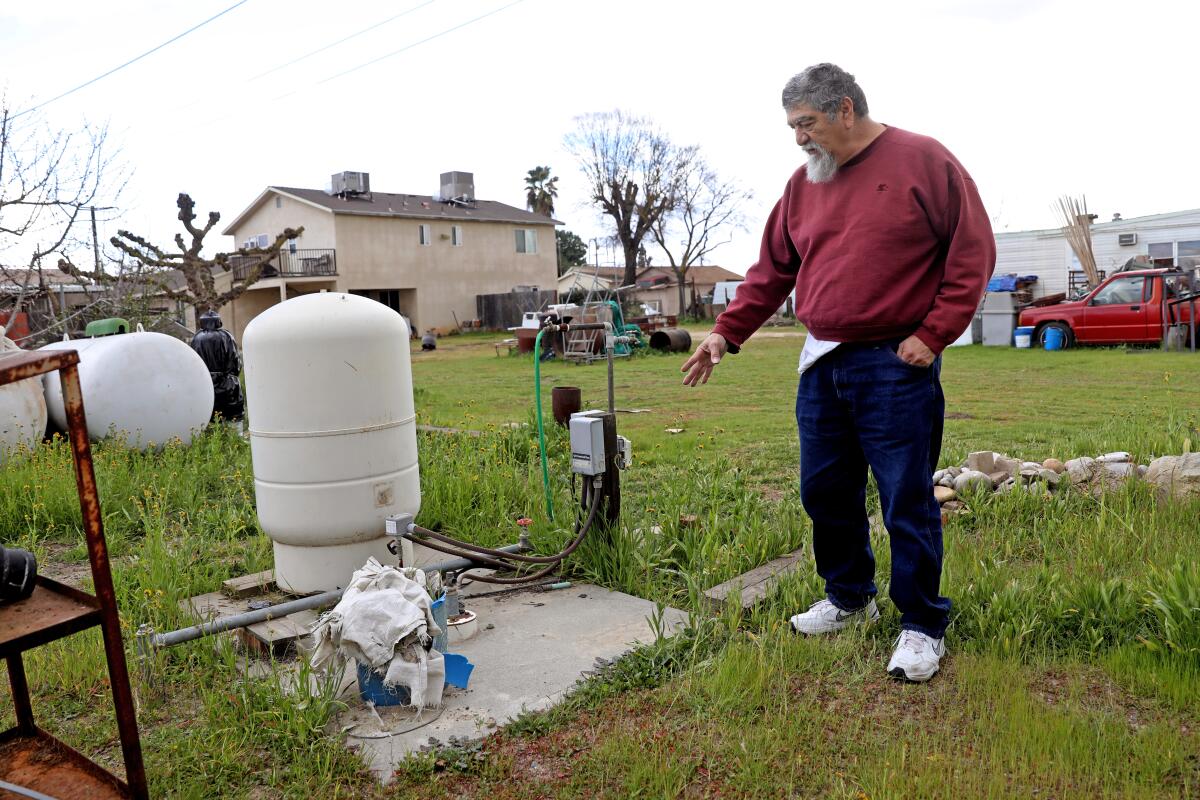 A man gestures toward a well in a grassy residential yard.