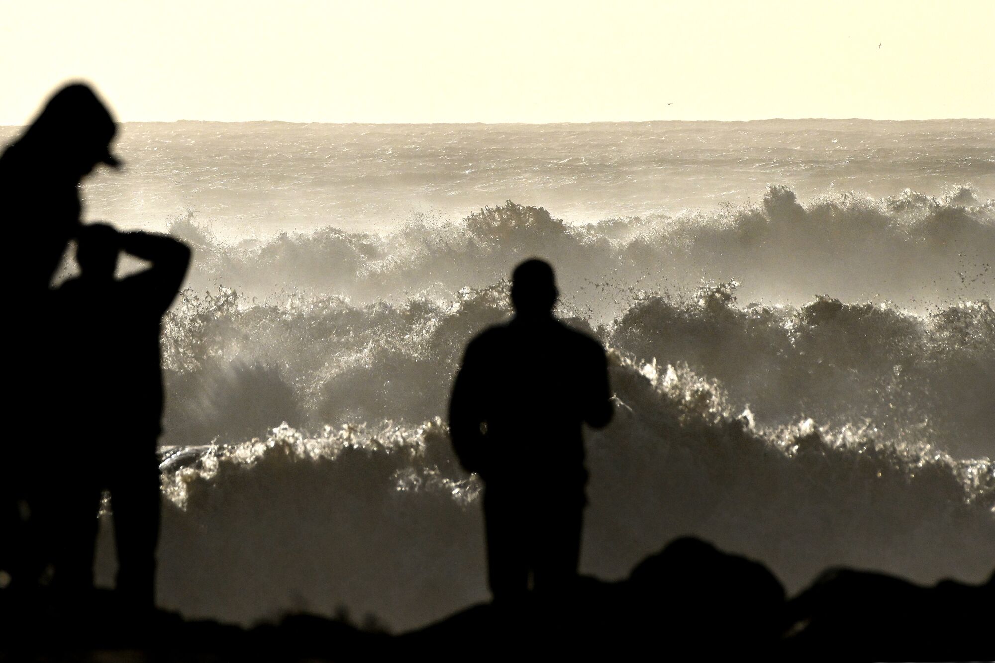 Silhouette of three people against high surf waves. 