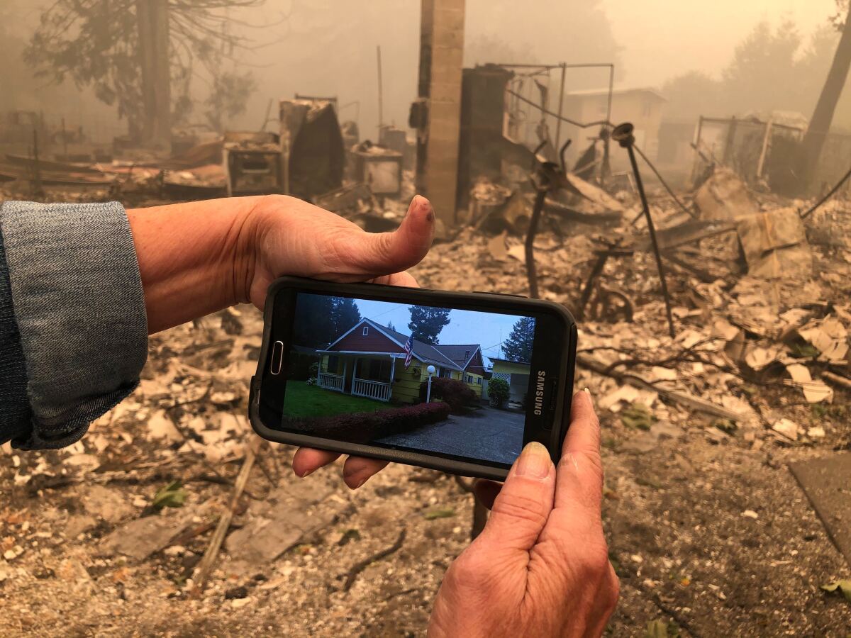 Mary Chenault holds a photo of her home in Lyons, Ore., before a wildfire reduced it to ruins.