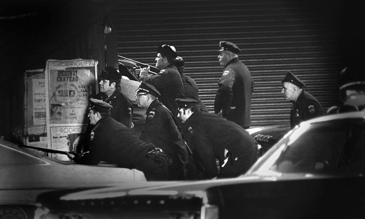 A black-and-white image of cops huddled behind cars.