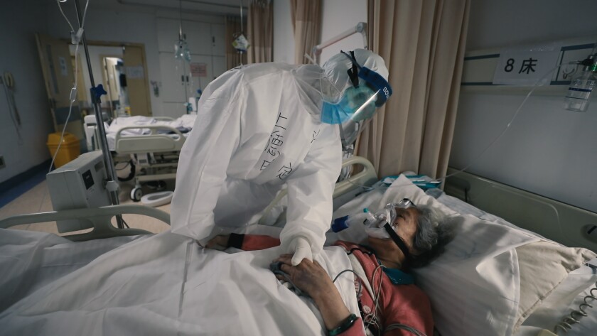 Paziente anziana di COVID-19, con un respiratore, confortata da un medico di Wuhan, in Cina.