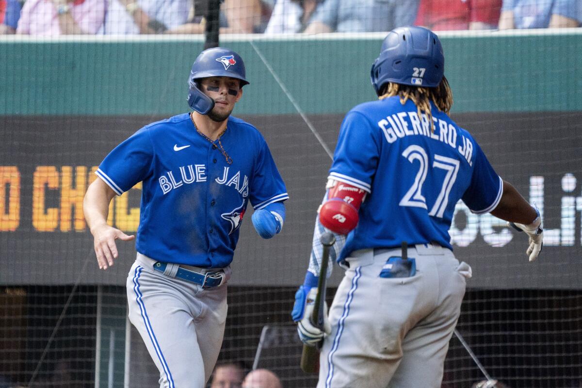 Toronto Blue Jays' Cavan Biggio, left, is congratulated by Vladimir Guerrero Jr. (27) after scoring on a ground ball by Teoscar Hernandez during the seventh inning of a baseball game against the Texas Rangers, Monday, April 5, 2021, in Arlington, Texas. Hernandez reached on an error by Rangers shortstop Charlie Culberson on the play. (AP Photo/Jeffrey McWhorter)