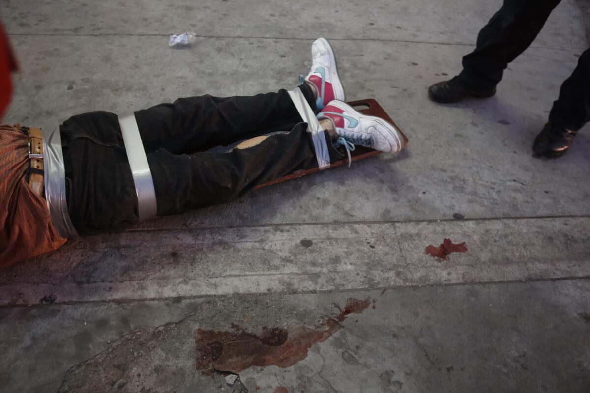 Red Cross paramedics tended to a man who is shot in the leg as a warning to pay his drug debts in the La Mesa neighborhood of Tijuana. He was strapped for transport.