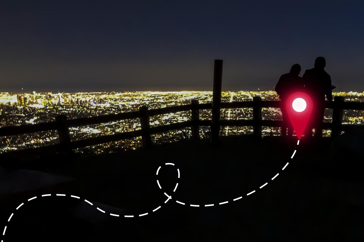 Two people and a low fence are silhouetted in the glow of city lights spread out in the background.