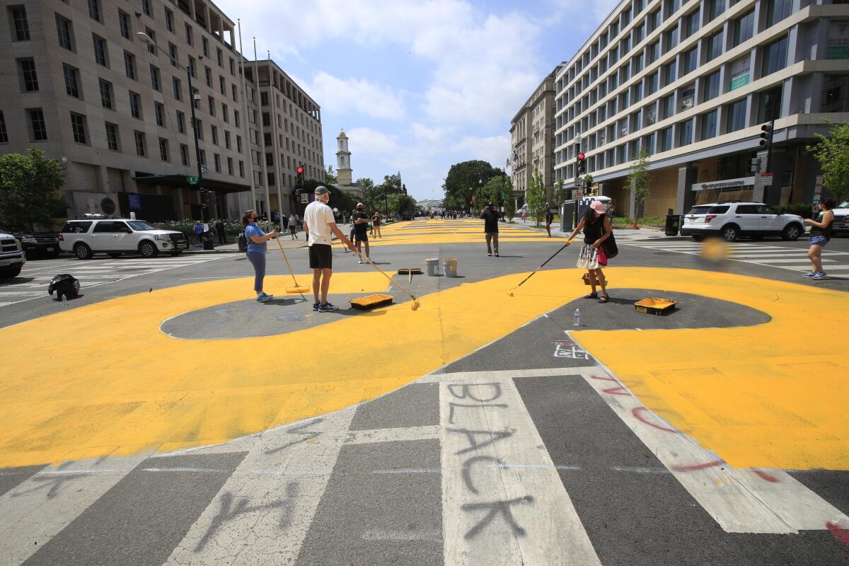 A group of people paints the words Black Lives Matter in enormous yellow letters on the street.