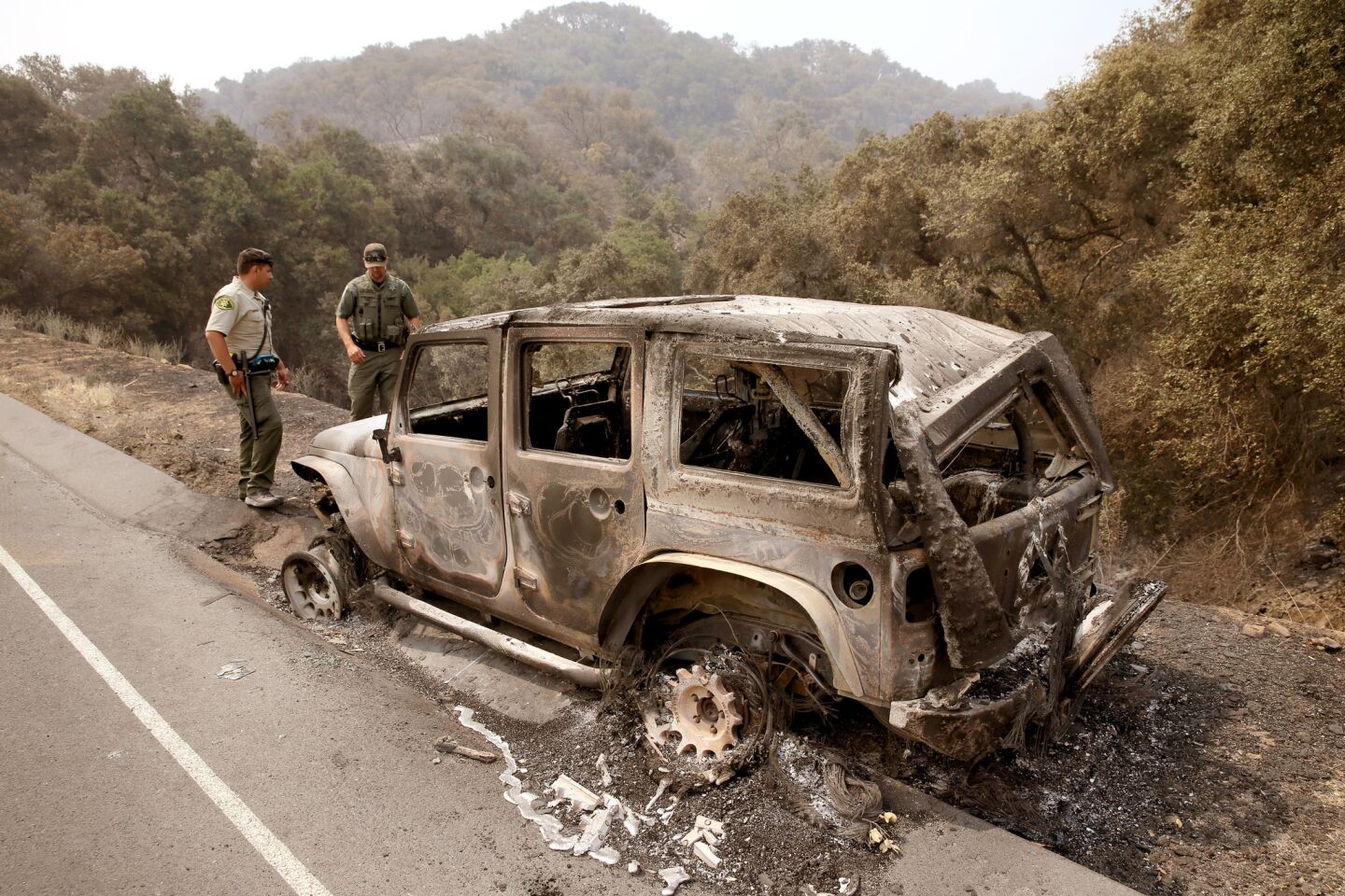 Santa Barbara Deputy Sheriff B. Bruening, left, and U.S. Fish & Wildlife game warden Max Magleby view a jeep that was abandoned and scorched by the Whittier fire along State Route 154 in the Los Padres National Forest near Lake Cachuma.