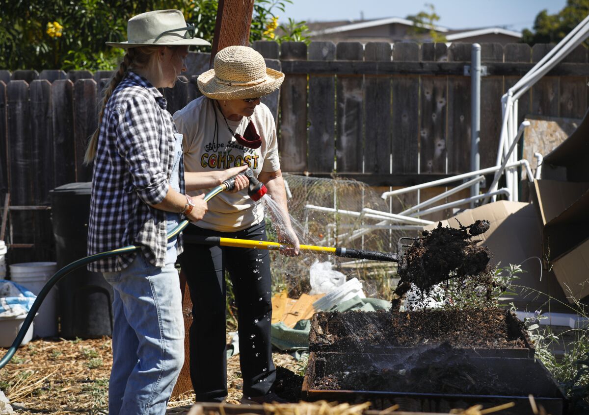 Alyssa Brodsky (left) wets down compost as volunteer Soil farmer Jill Selders uses a pitch fork to turn and move the compost.