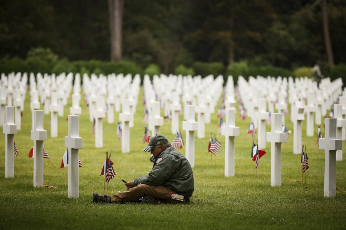 Man sitting among rows of white crosses in cemetery