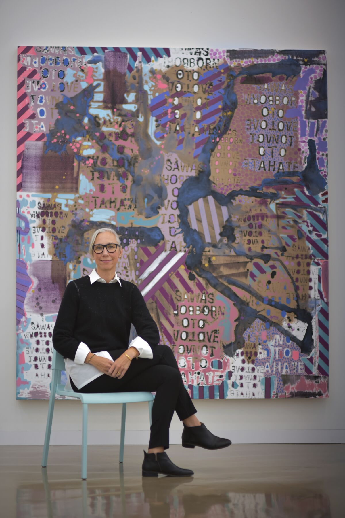 A woman sits on a chair in front of a painting 