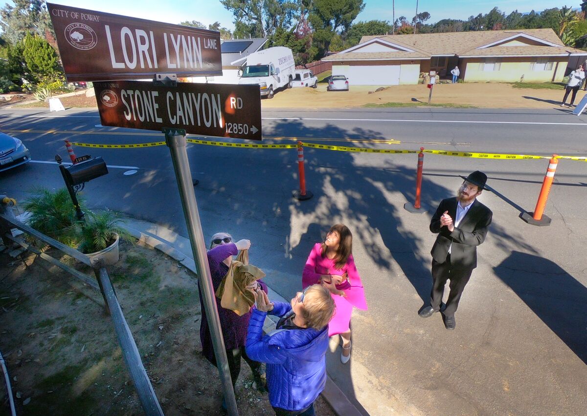 Four people, including a rabbi in black hat, look up at crossing street signs for Lori Lynn Lane and Stone Canyon Road.