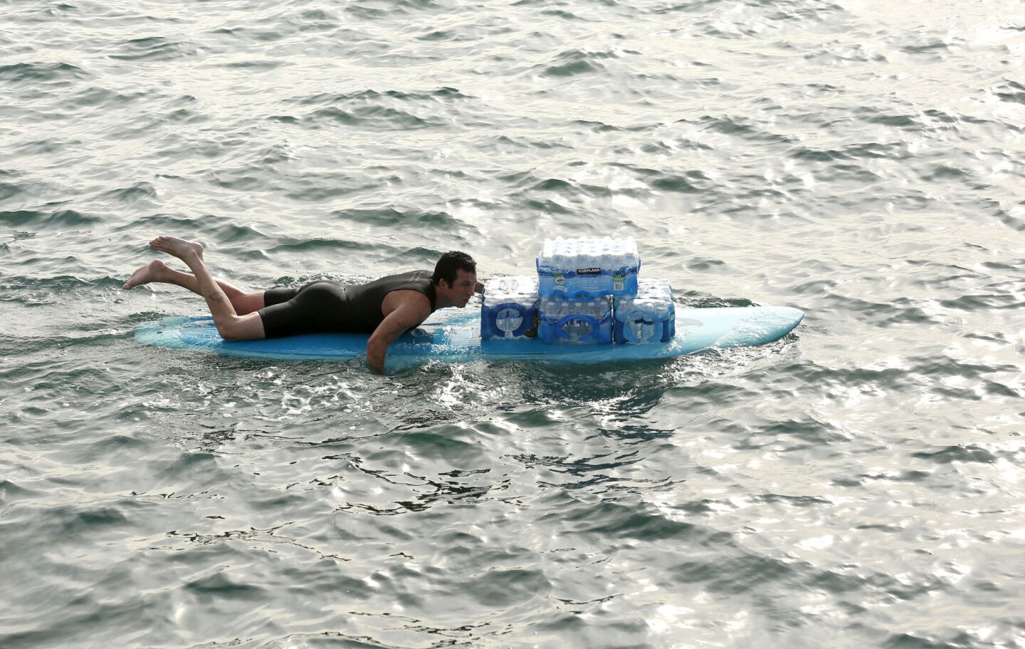 A man ferries cases of water by surfboard to help residents in the Paradise Cove area of Malibu.