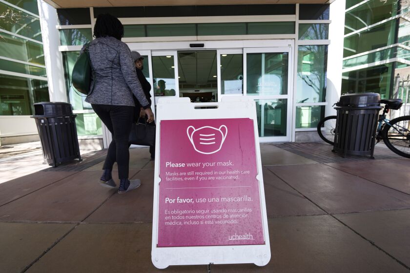 FILE - A sign advising visitors to don face coverings stands outside the main entrance to UCHealth University of Colorado hospital Friday, April 1, 2022, in Aurora, Colo. COVID cases are starting to rise again in the United States, with numbers up in most states and up steeply in several. One expert says he expects more of a “bump” than the monstrous surge of the first omicron wave, but another says it’s unclear how high the curve will rise and it may be more like a hill. (AP Photo/David Zalubowski, File)