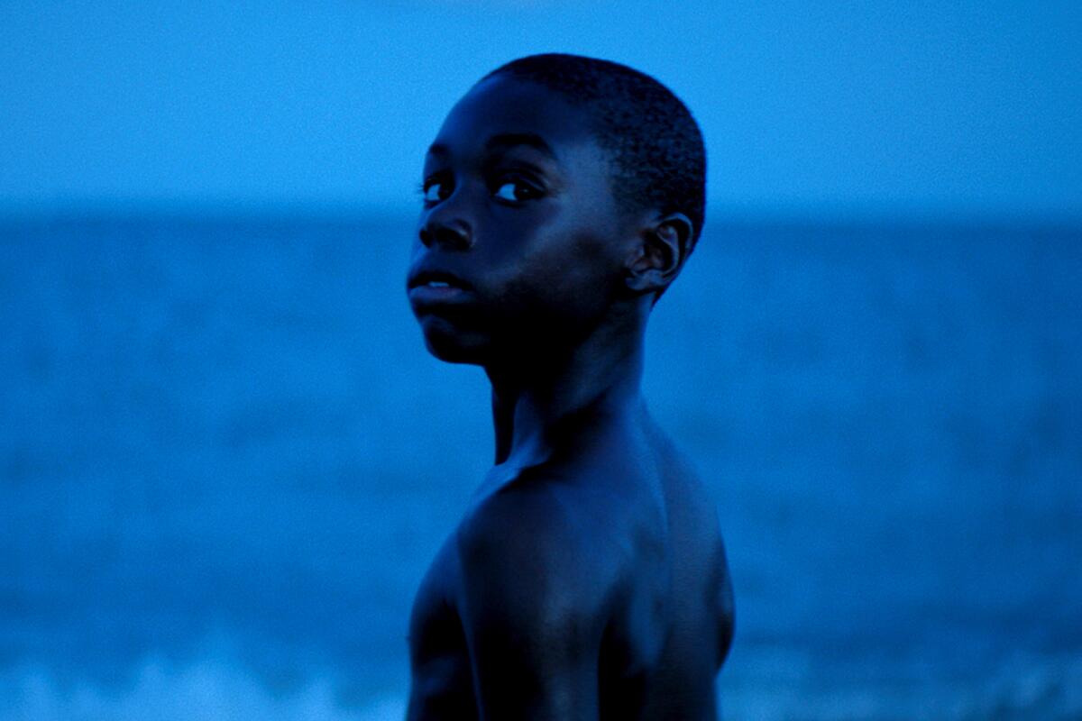 With the ocean as his backdrop, a Black boy bathed in blue light looks toward the camera in a scene from "Moonlight." 