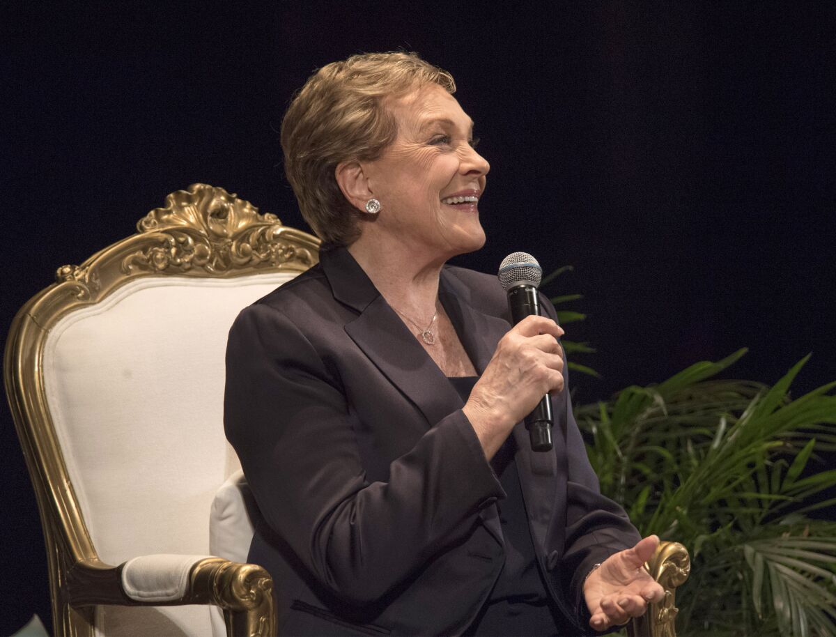 Julie Andrews, smiling and holding a microphone, seated onstage at the Orpheum.