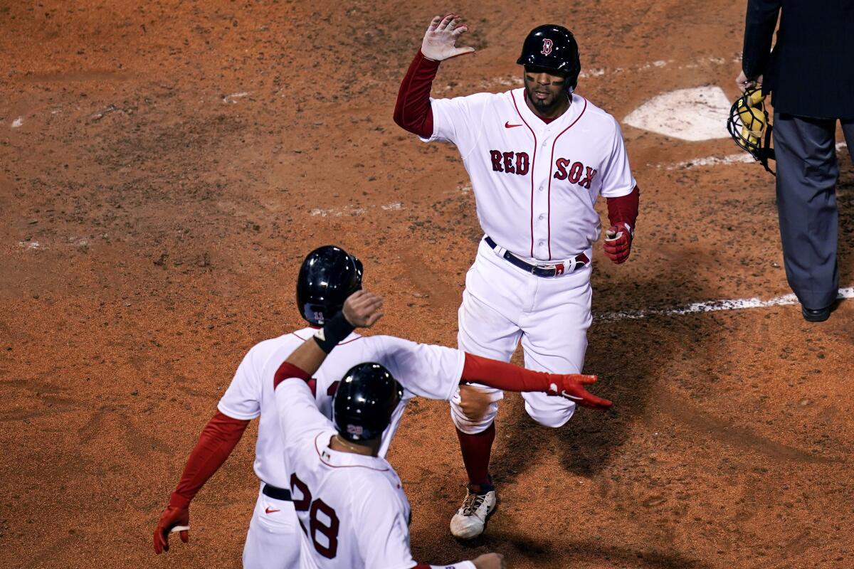 Boston Red Sox's Xander Bogaerts, top, is congratulated by Rafael Devers, center, and J.D. Martinez (28) after scoring on his own double following a throwing error by Tampa Bay Rays catcher Mike Zunino, during the fifth inning of a baseball game at Fenway Park, Monday, April 5, 2021, in Boston. (AP Photo/Charles Krupa)