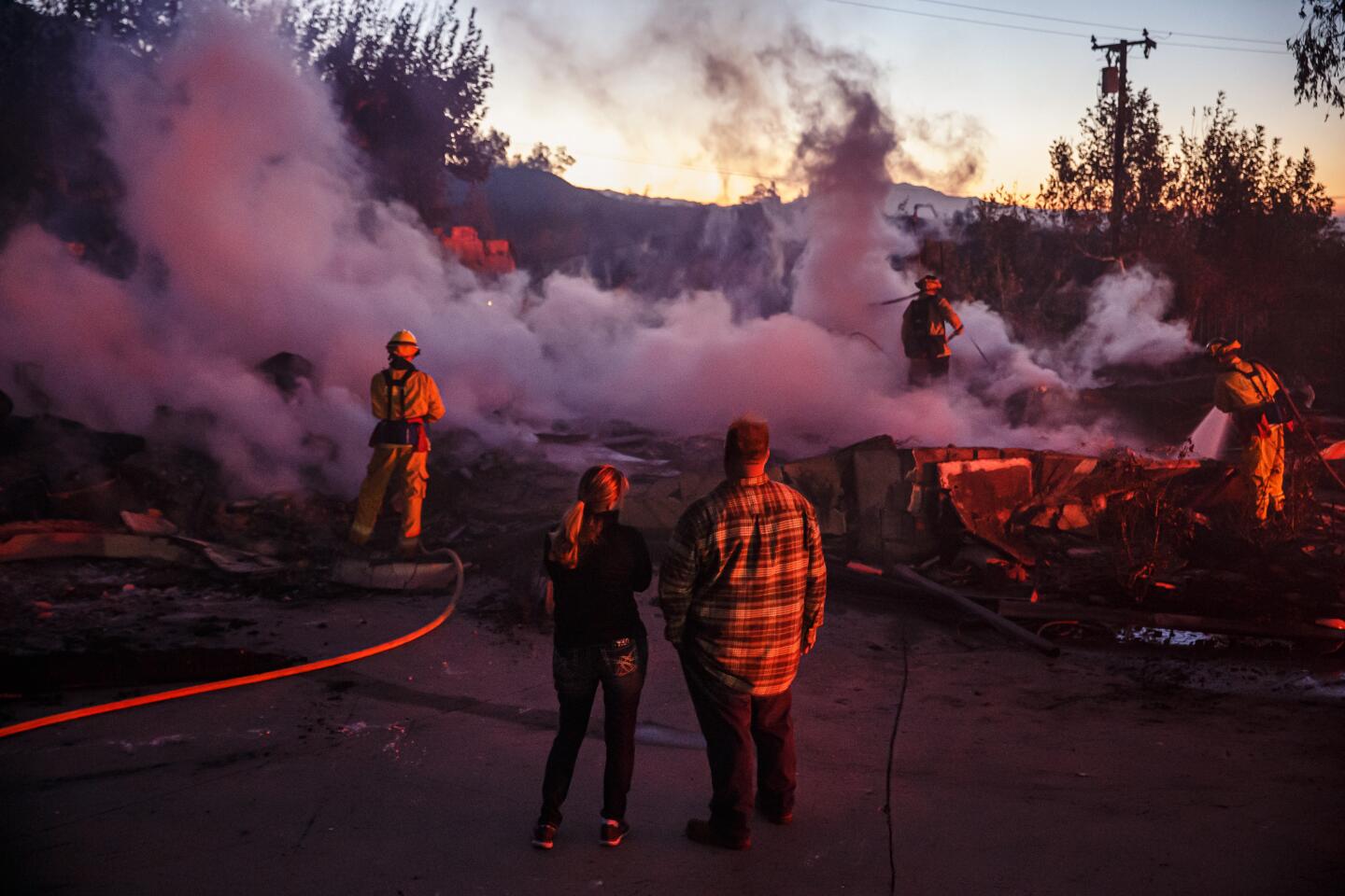 SAN BERNARDINO, CALIF. -- THURSDAY, OCTOBER 31, 2019: Family members look on as firefighters mop up a burned down home destroyed by the Hillside Fire in San Bernardino, Calif., on Oct. 31, 2019. (Marcus Yam / Los Angeles Times)