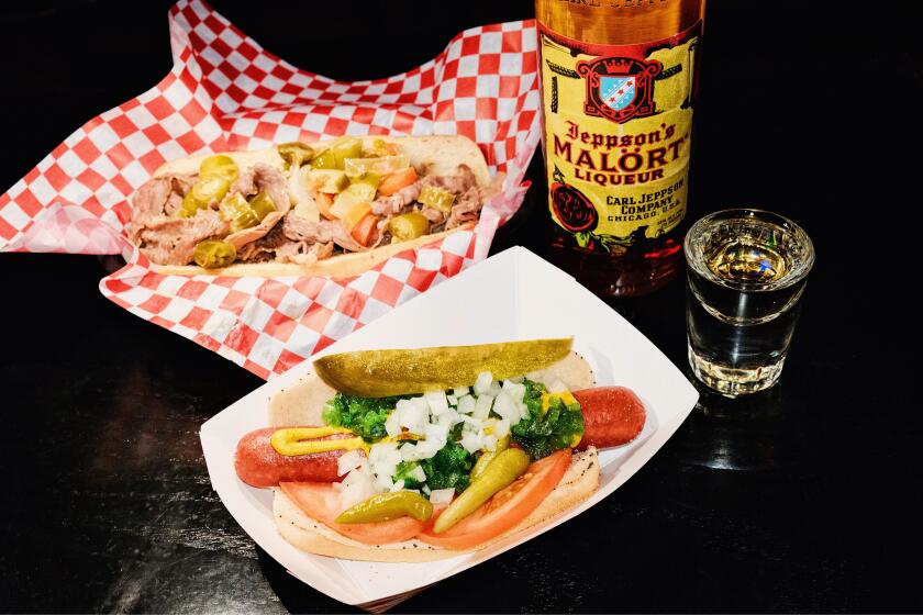 An Italian beef sandwich with a Chicago dog and a bottle and shot of Jeppson's Malört on a black table at Tiny's Hi-Dive.