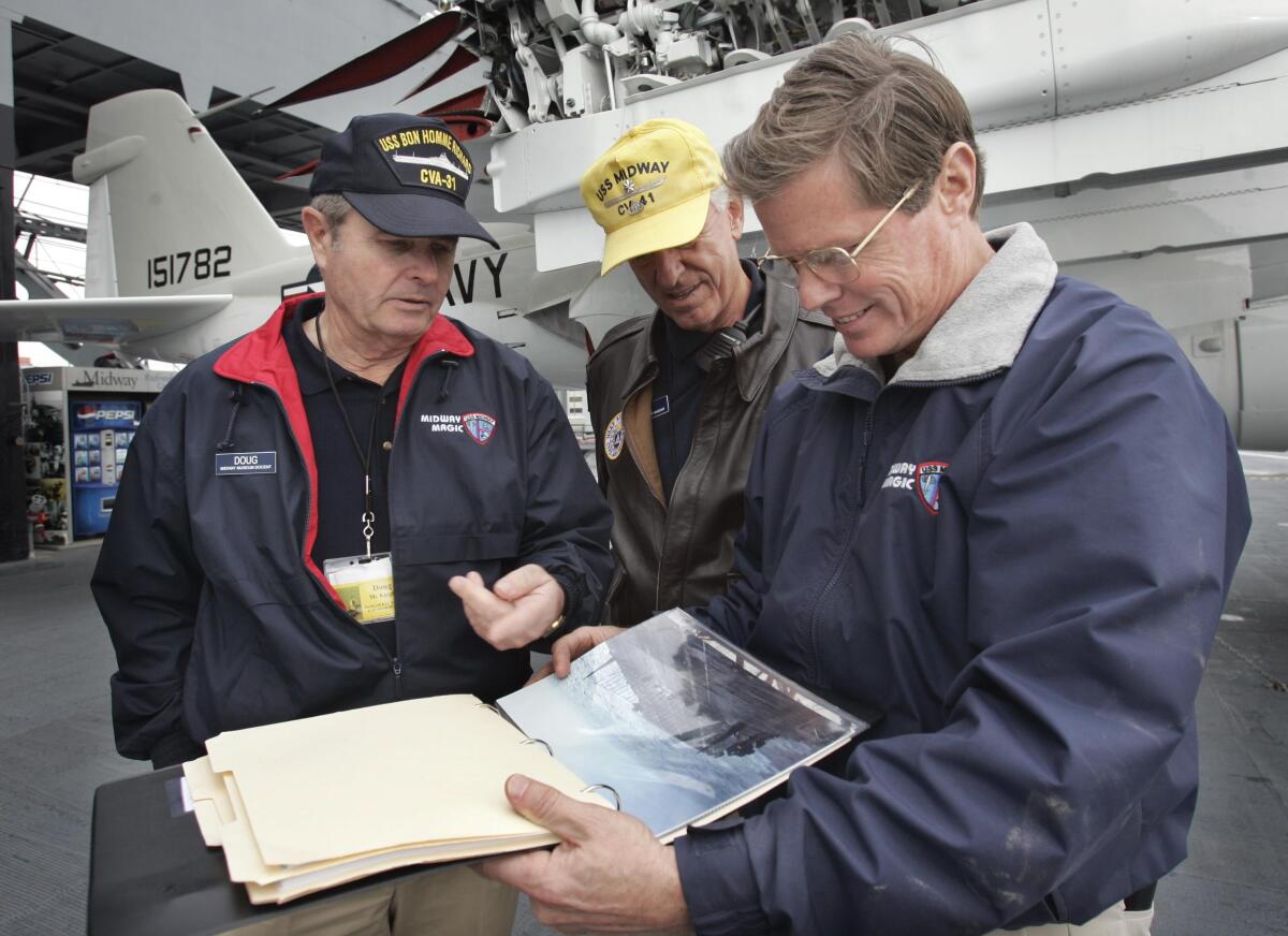 Volunteer Doug McKnight, left, shows old aircraft photos to volunteer Jim Nash, center, and CEO Mac McLaughlin.
