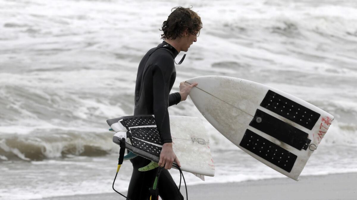 A surfer walks out of the water with a broken board after surfing at Zuma Beach in Malibu in 2016.