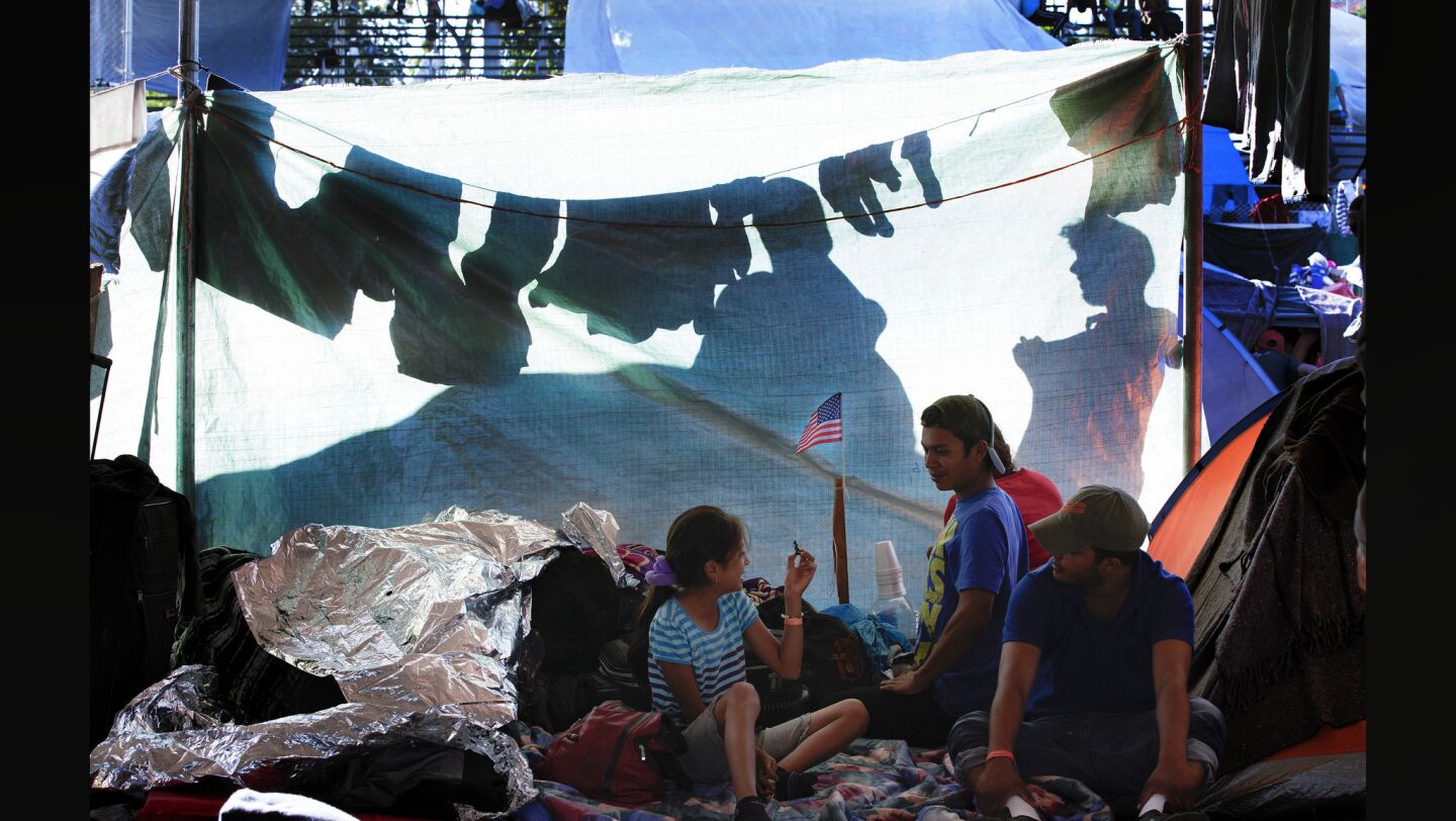 At the temporary shelter set in the Benito Juarez Sports Complex in Tijuana, a family relaxes under a the large tent as two others hang fresh wet laundry outside to dry.