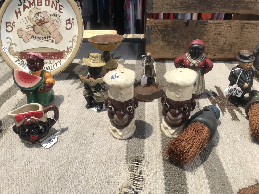 About a dozen anti-Black figurines sit on a table including saltshakers, a mug and plate.