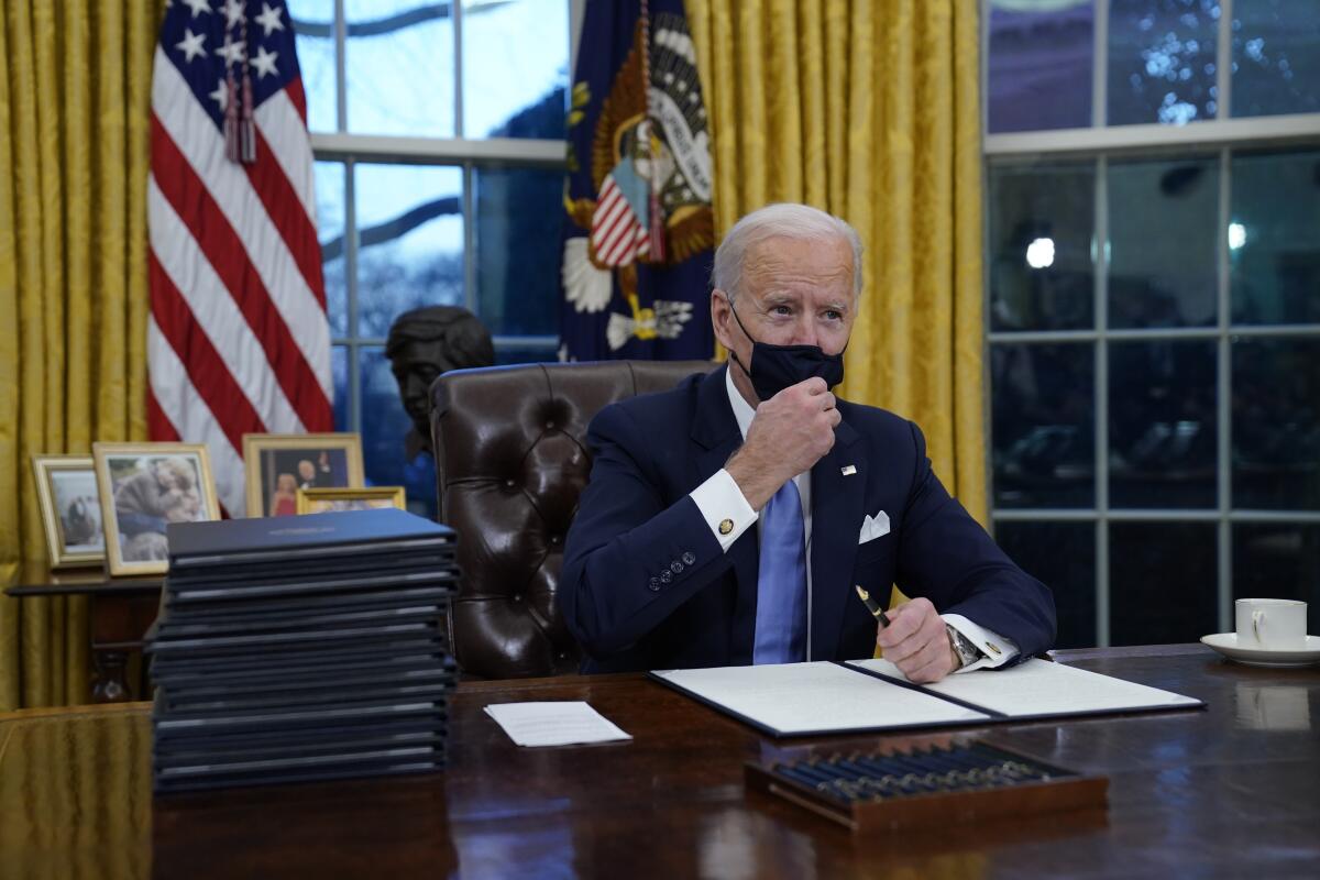 President Biden adjusts his face mask as he signs his first executive orders in the White House on Jan. 20.