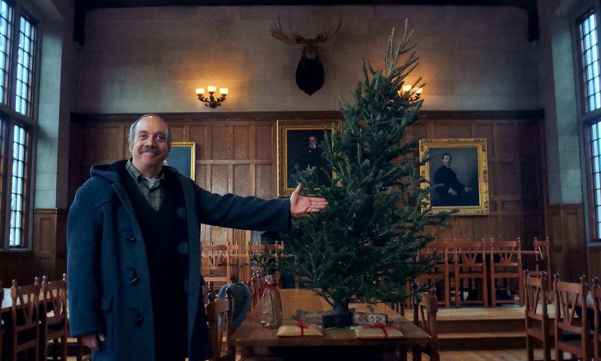 A smiling man gestures proudly at a tilted Christmas tree in "The Holdovers."