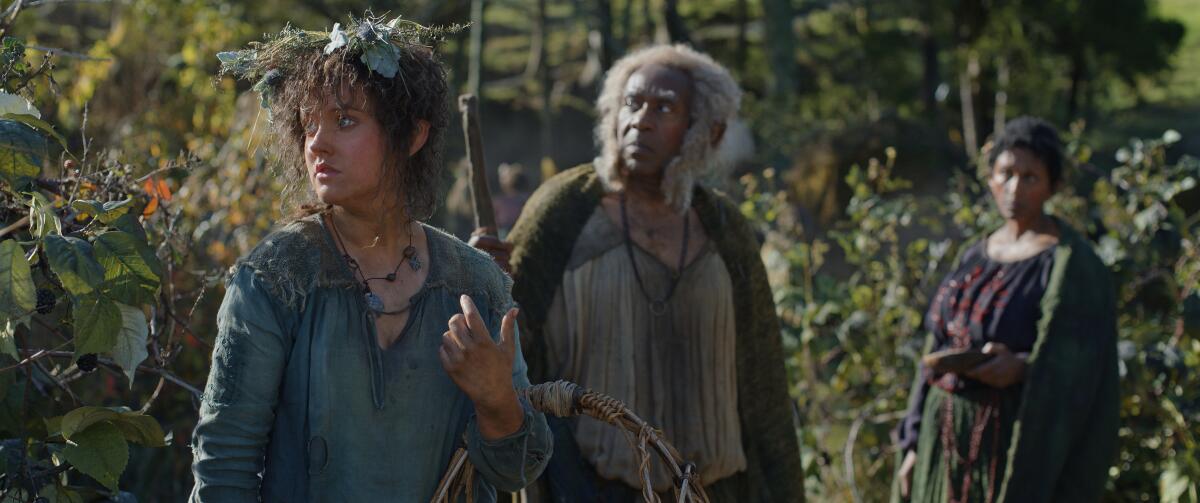 A young woman with plants in her hair standing near a man and another  woman.