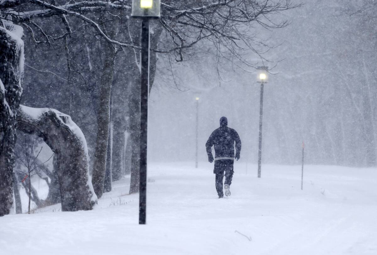 Una persona hace ejercicio trotando durante una fuerte nevada con la iluminación callejera encendida.