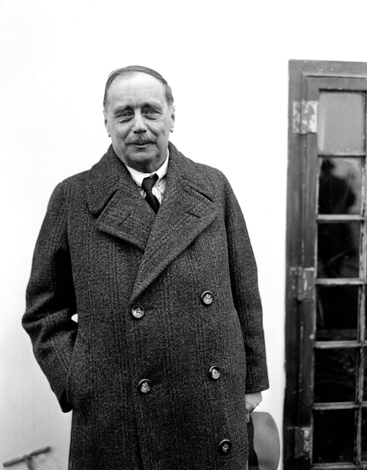 A black and white photo of author H.G. Wells in a long, double-breasted coat 