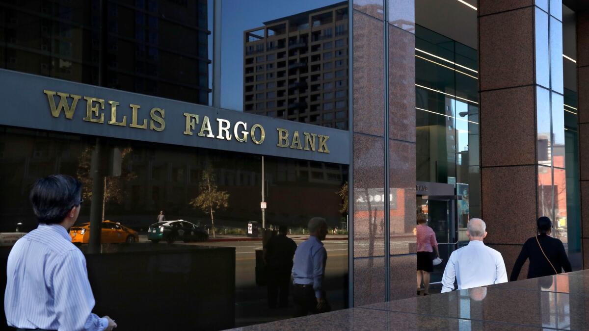 Pedestrians walk past a Wells Fargo bank located at Wells Fargo plaza on 333 S Grand Ave. in downtown Los Angeles on Monday. Wells Fargo stock plunged after the Federal Reserve hit the bank with new sanctions Friday over its fake accounts scandal and other wrongdoing.
