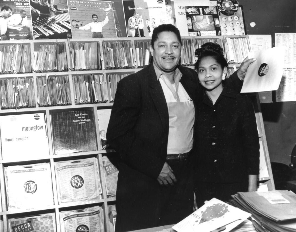 A man and woman stand in front of a record store display in a black and white image
