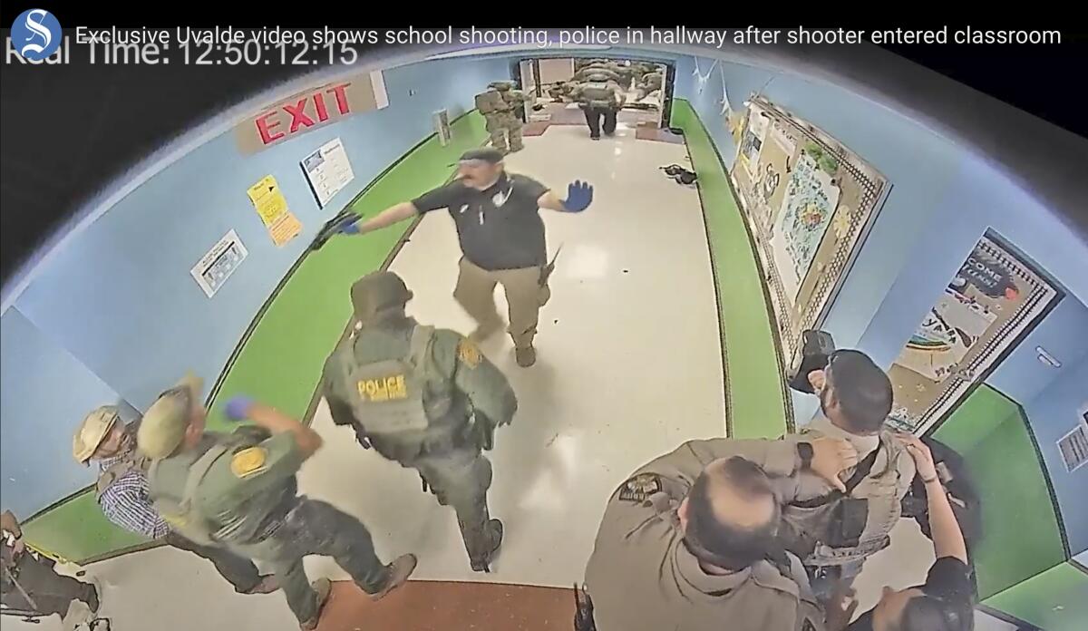 In a photo from surveillance video, more than 10 law enforcement officers stand or walk in a school hallway.  