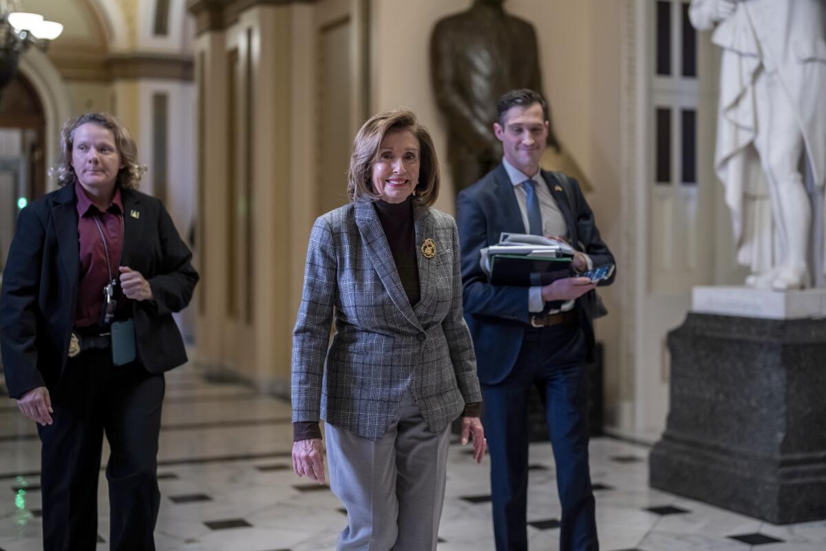 Speaker of the House Nancy Pelosi walks through a hall with two people behind her.