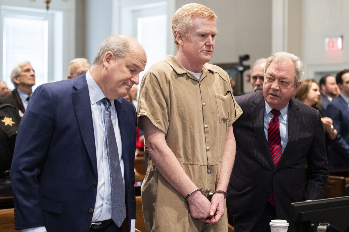 Alex Murdaugh, handcuffed and wearing a tan jail jumpsuit, stands with his legal team in court.