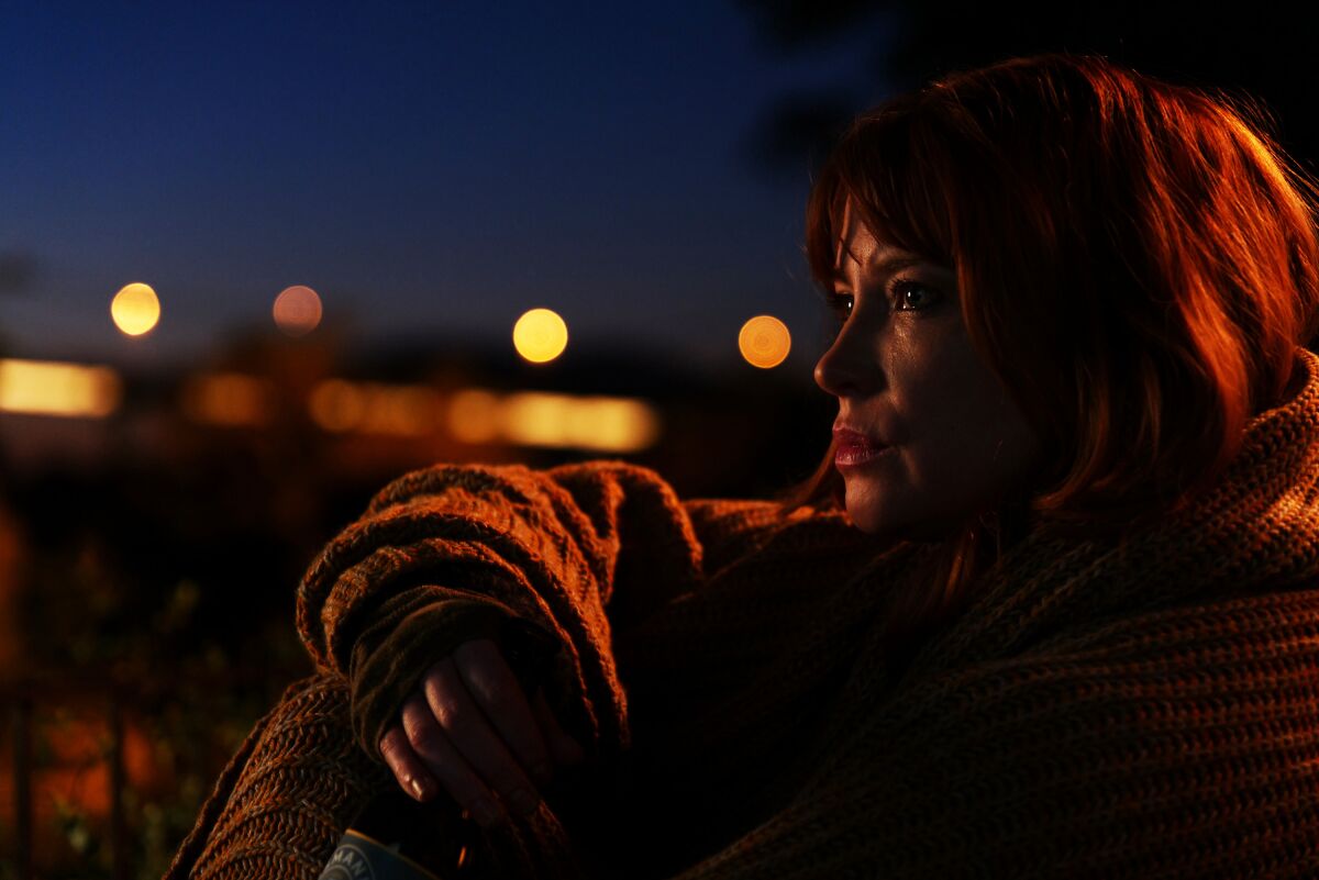 A closeup of a woman sitting outside at night looking contemplative.