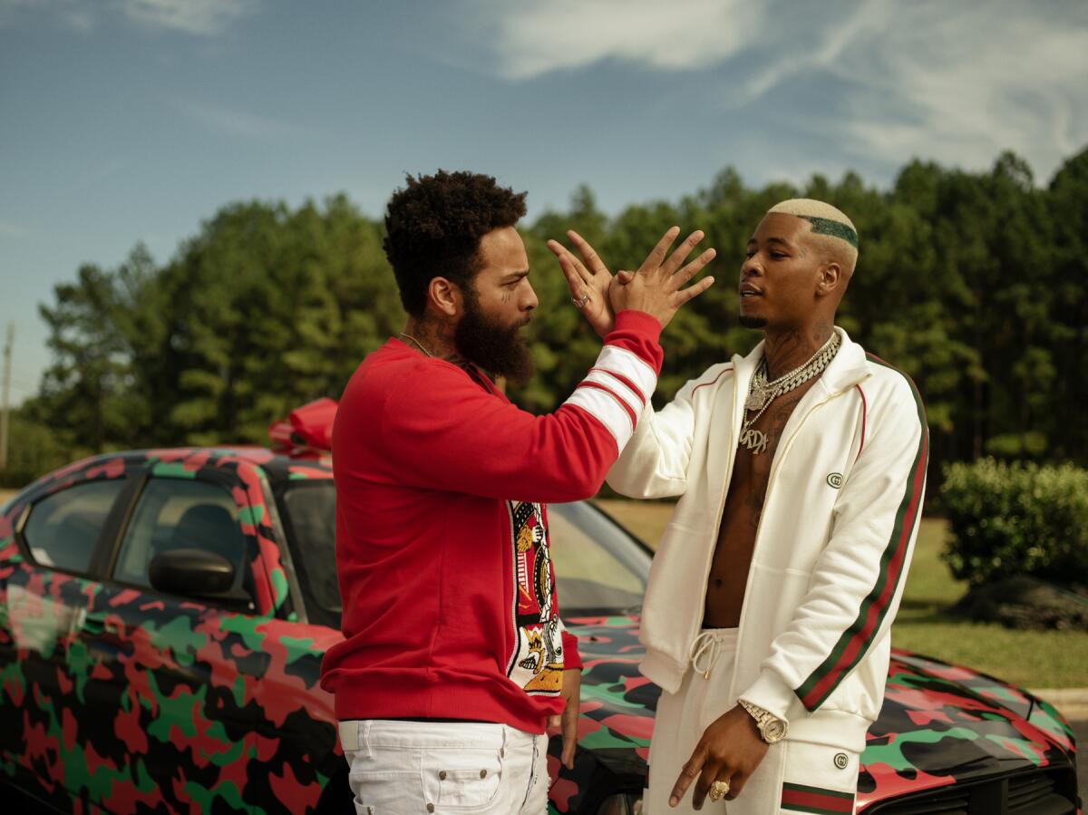 A man wearing a red sweater and a man in a white sweatsuit clasp hands.