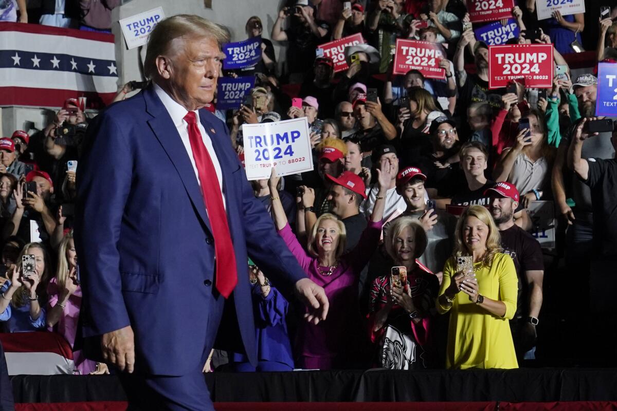 Former President Trump walking in front of a crowd of supporters, many with "Trump 2024" signs.