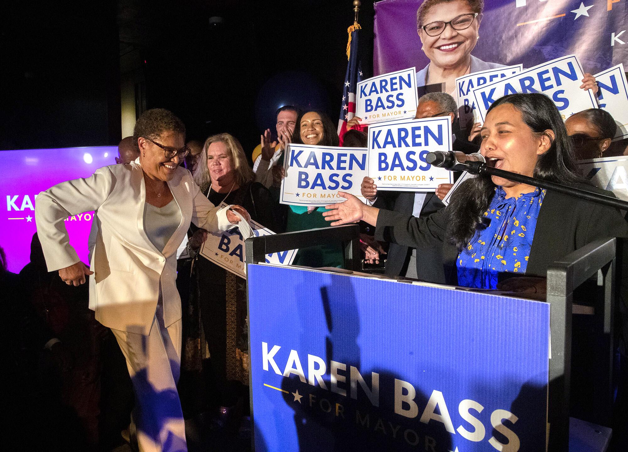 Karen Bass striding to the microphone as a speaker introduces her and others raise campaign signs