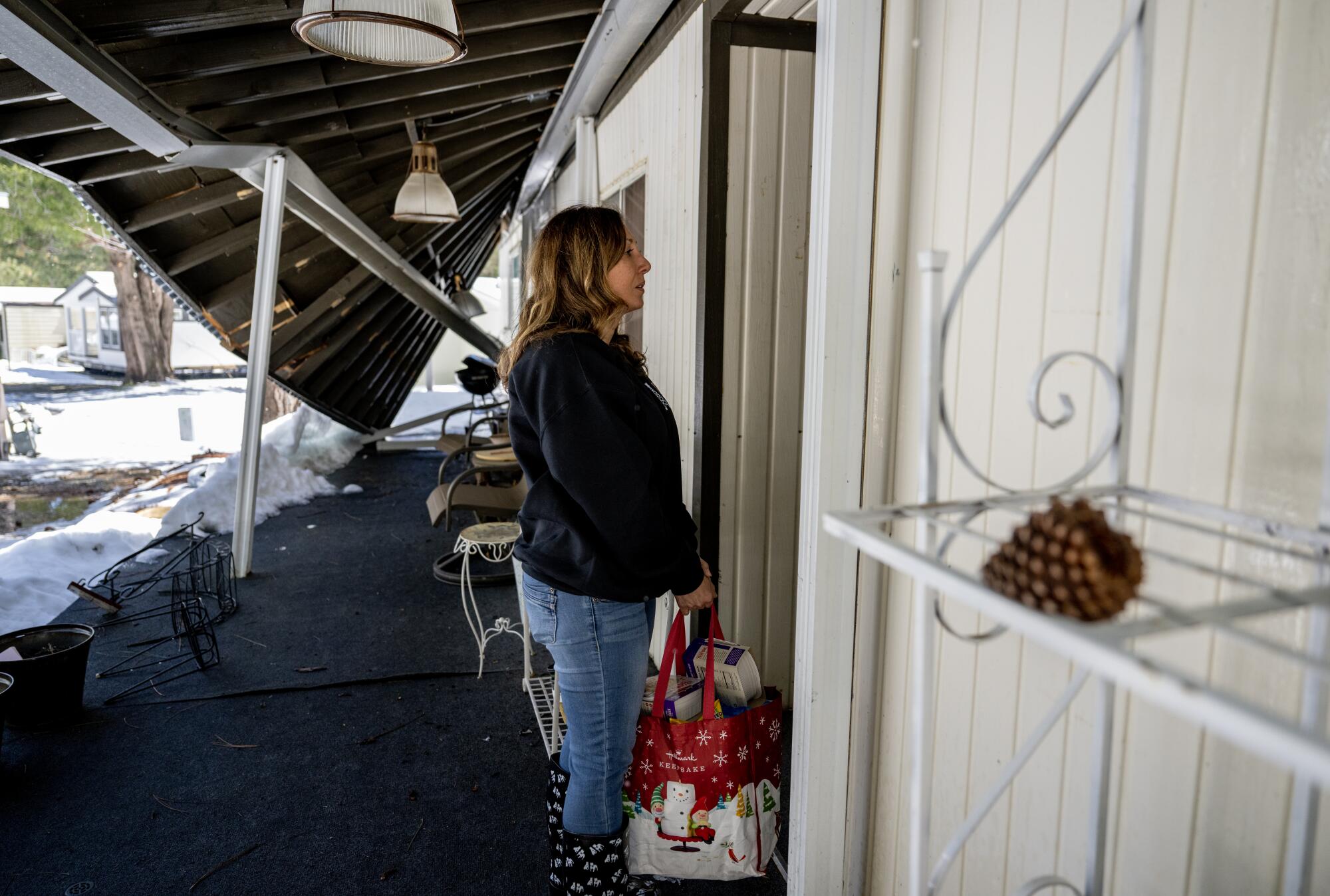 A woman holds a bag as she stands in front of the door of a home with a partially collapsed awning.