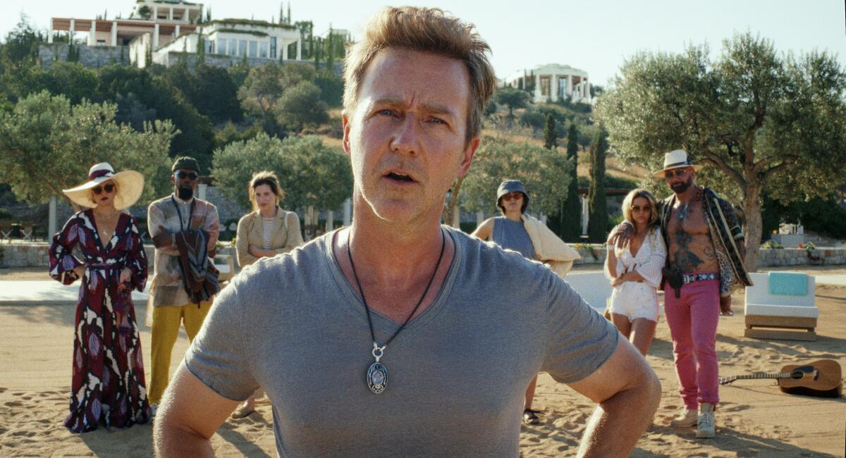 A man in a gray T-shirt, hands on his hips, stands with several people behind him on a beach.