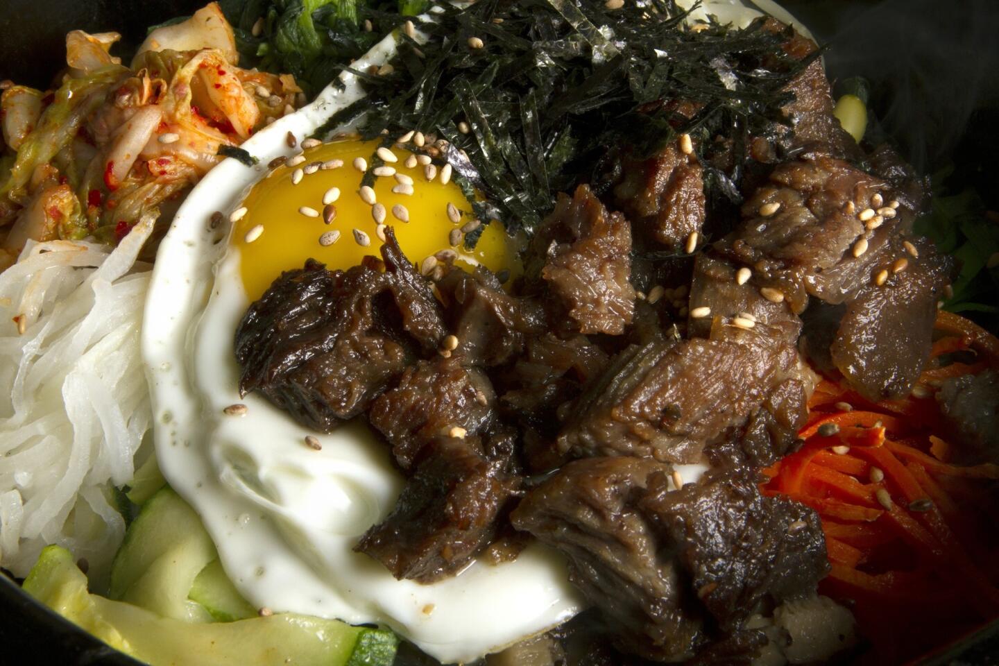 The beef bibimbap is served in a black pot at Jeonju Dolsot in Los Angeles. The pot includes rice topped with kimchi, assorted vegetables and seaweed. It also comes with seaweed soup, noodles in young radish, Korean pancake, dried shrimp with soy bean, squash and cabbage with bean paste.