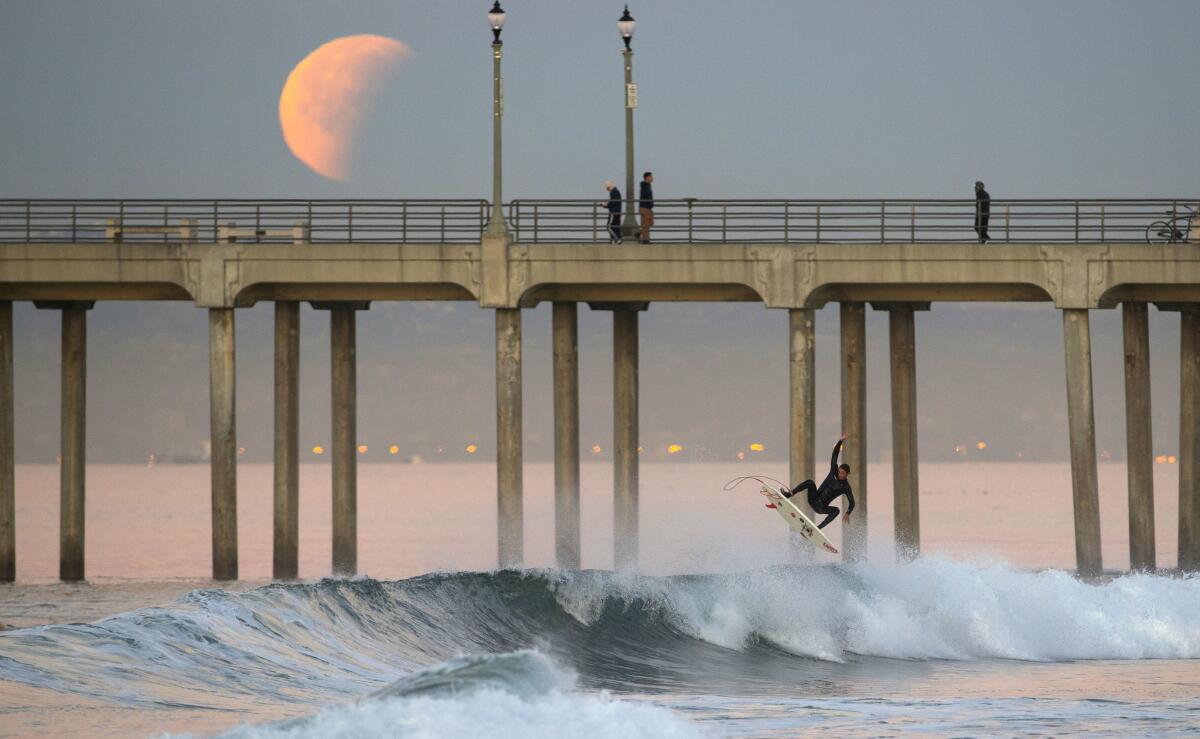 Surfer Chris Mansor goes airborne off a wave as the super blue blood moon eclipse sets over the Huntington Beach pier.