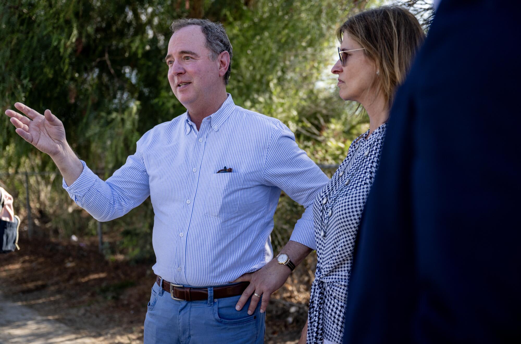 Adam Schiff standing next to a woman outdoors, gesturing as he speaks to people outside the frame