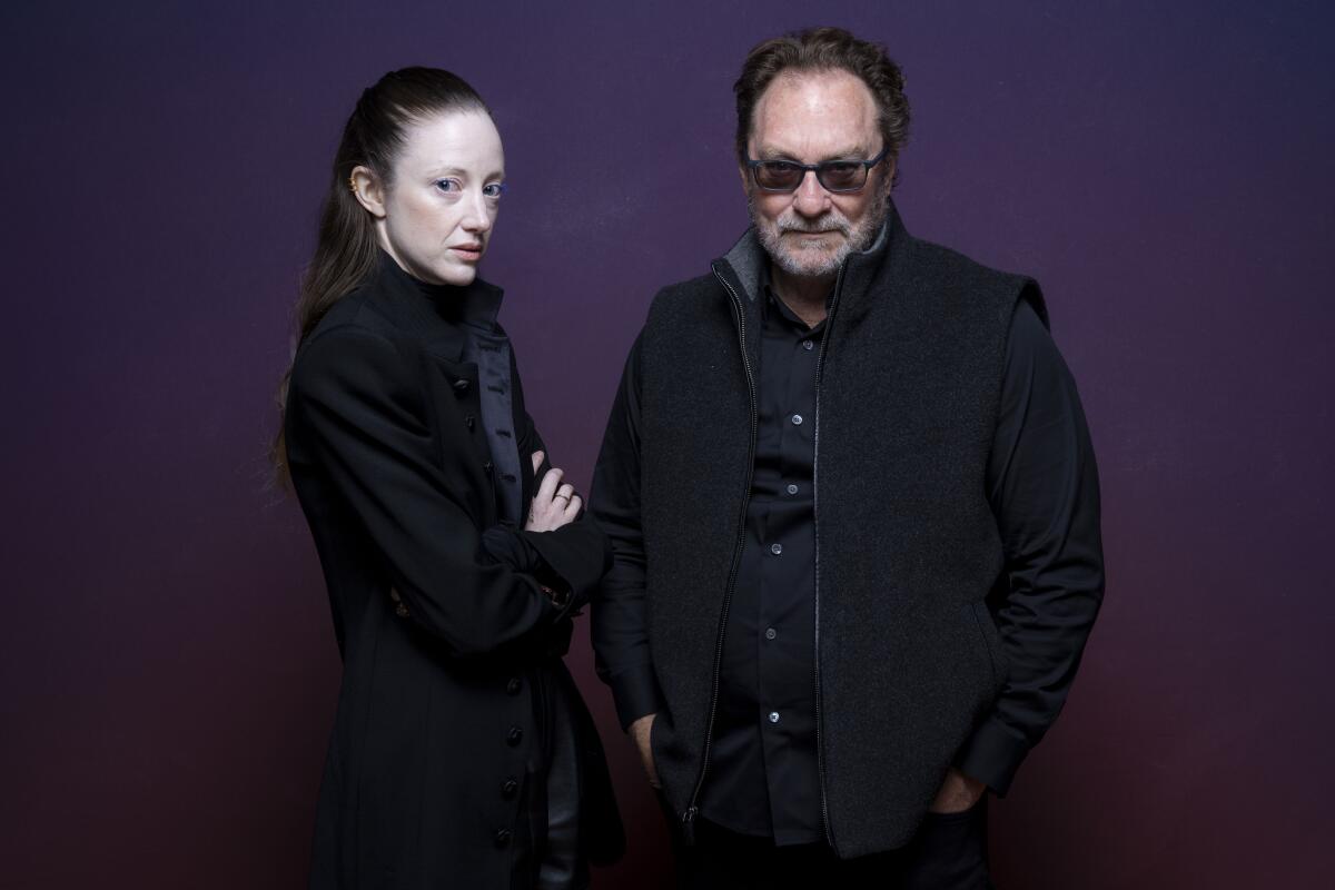 A woman and a man in dark glasses stand together.