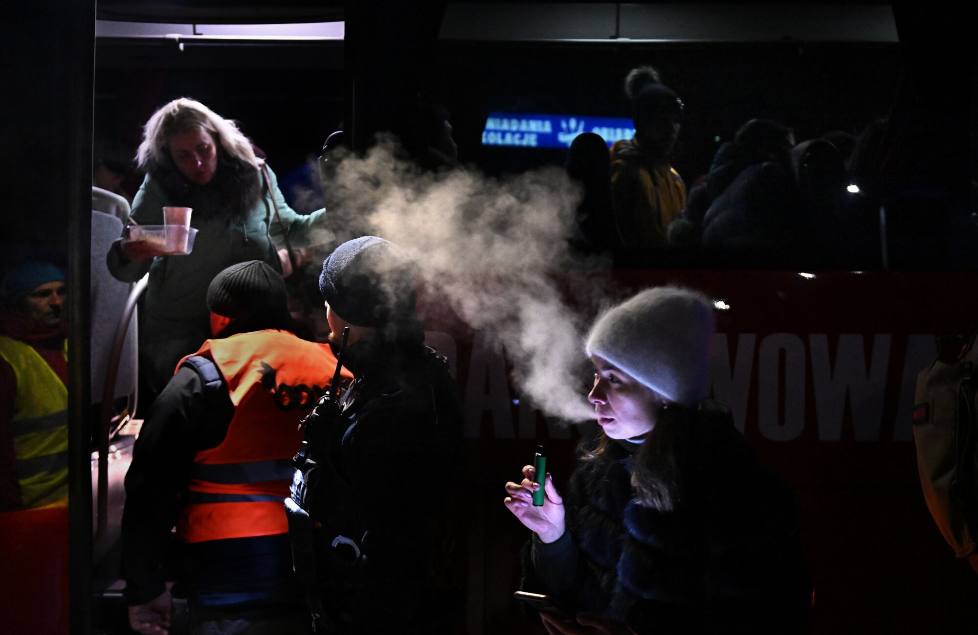 A woman smokes in front of a bus carrying refugees.